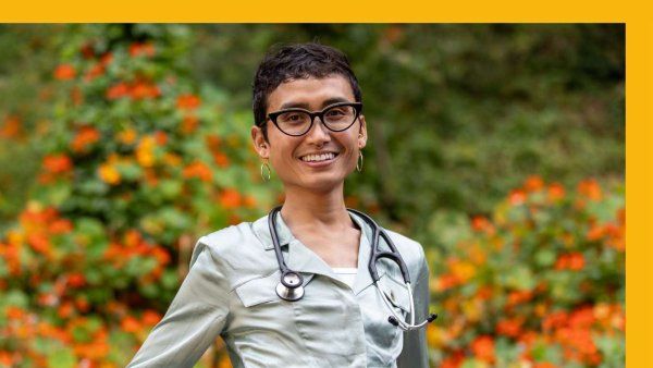 Sen wears stethoscope and poses in front of flowers.