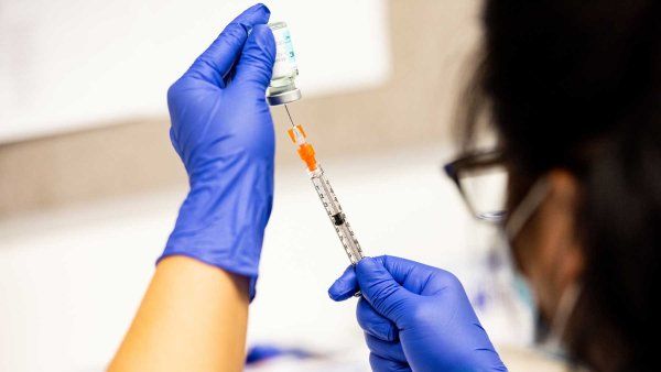 A pharmacy technician wearing blue latex glove and a surgical mask prepares a dose of the Moderna COVID-19 vaccine.