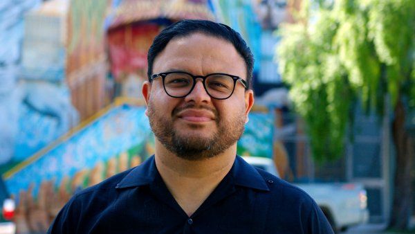 Manuel Tapia looks ahead against the backdrop of a colorful blue building in the Mission.