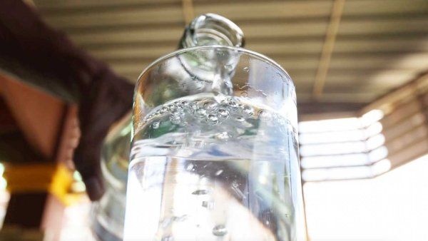 A hand pouring water into a glass from a bottle.