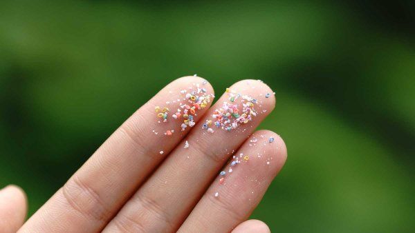 A closeup of fingertips holding microplastic particles.