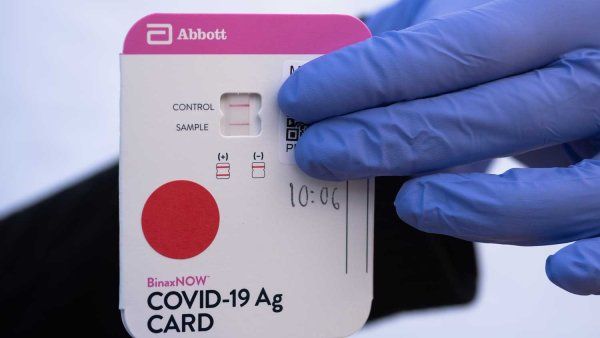 Two gloved hands hold a rapid antigen test card showing a positive COVID-19 result.