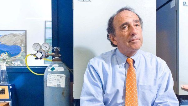 Scientist sits stylishly in yellow tie next to air tank in laboratory.