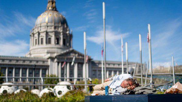 A homeless elderly man sleeps on a bench outside of San Francisco City Hall.