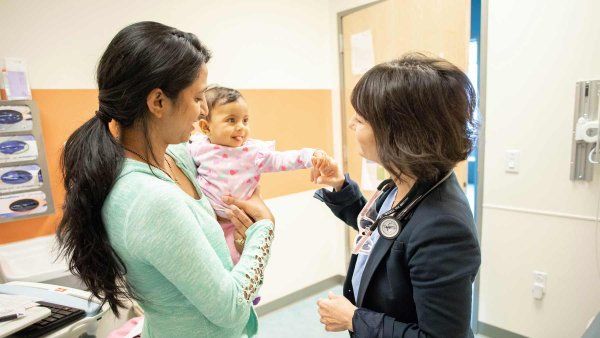 A mother holds a smiling baby as Dr. Paula Price shakes the baby's hand.