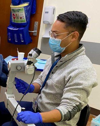 Nurse practitioner Vasean Patel wears latex gloves and a surgical mask as he performs an exam using an anoscope and colposcope to screen for anal HPV-related disease.