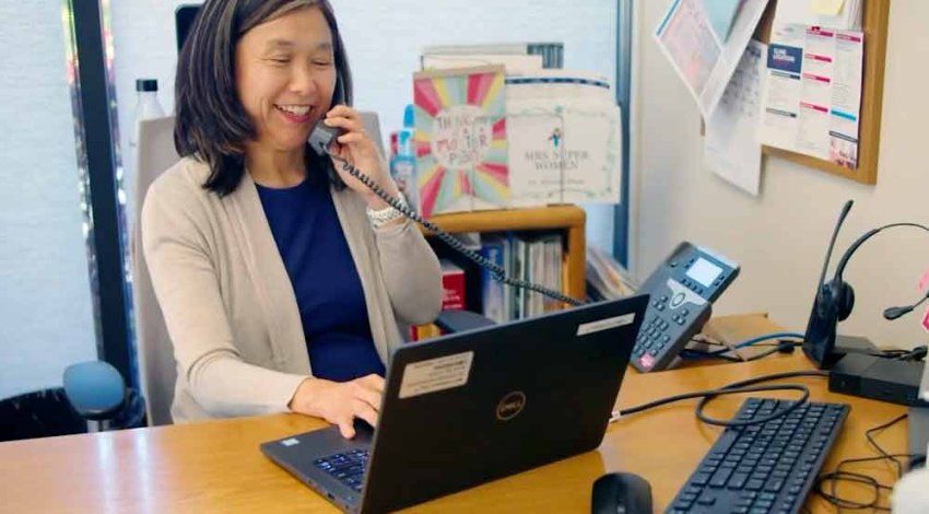 Miriam Rhew smiles as she consults with someone on a phone and looks at her laptop.