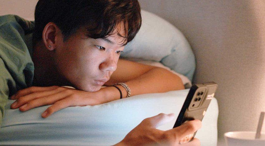 A teenage boy looking at his phone at night.