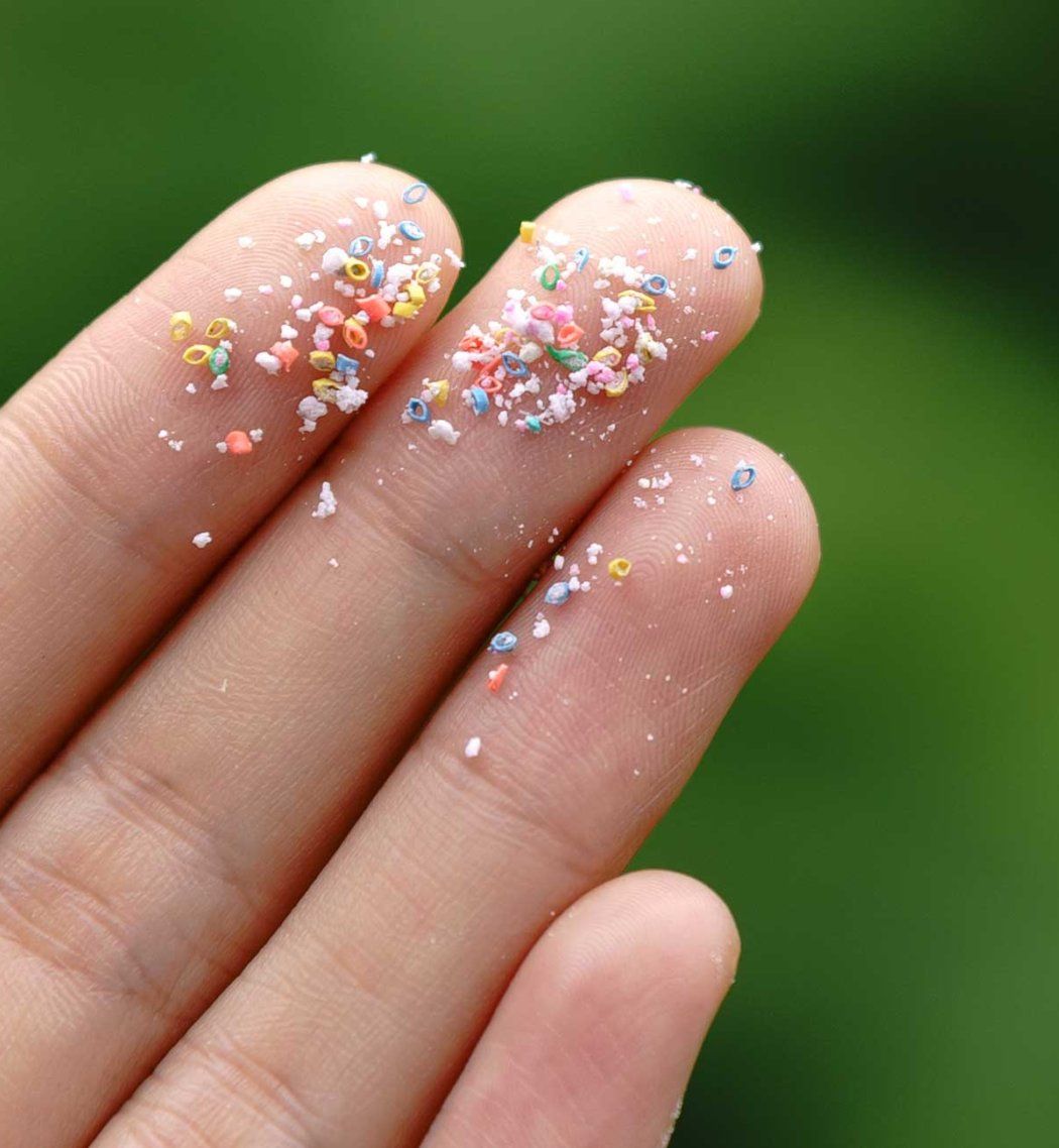 A closeup of fingertips holding microplastic particles.