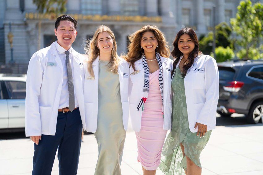 Four new students donning white coats smile and pose.